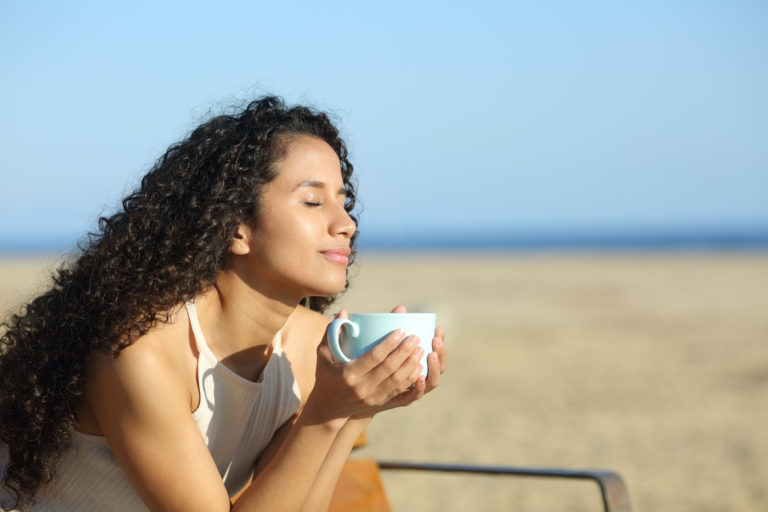 Latin woman enjoying a cup of coffee on the beach