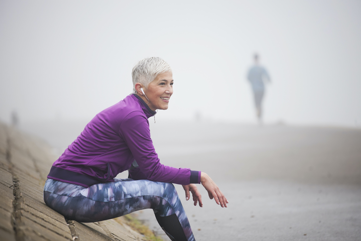 Beautiful mature woman jogging through fog in early autumn day