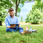 Happy young man using tablet while sitting outdoor in the park