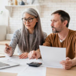 Mature middle-aged couple family wife and husband counting funds, savings declarations, investments,paperwork, financial documents, bankruptcy, court case, bills, pension with laptop.