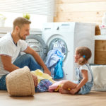 Happy family man father householder and child in laundry with washing machine