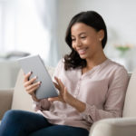 Smiling young woman on couch using tablet