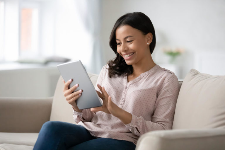 Smiling young woman on couch using tablet