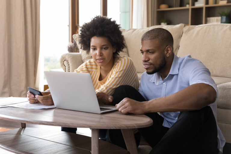 Young couple looking at a computer screen and managing finances together at home.
