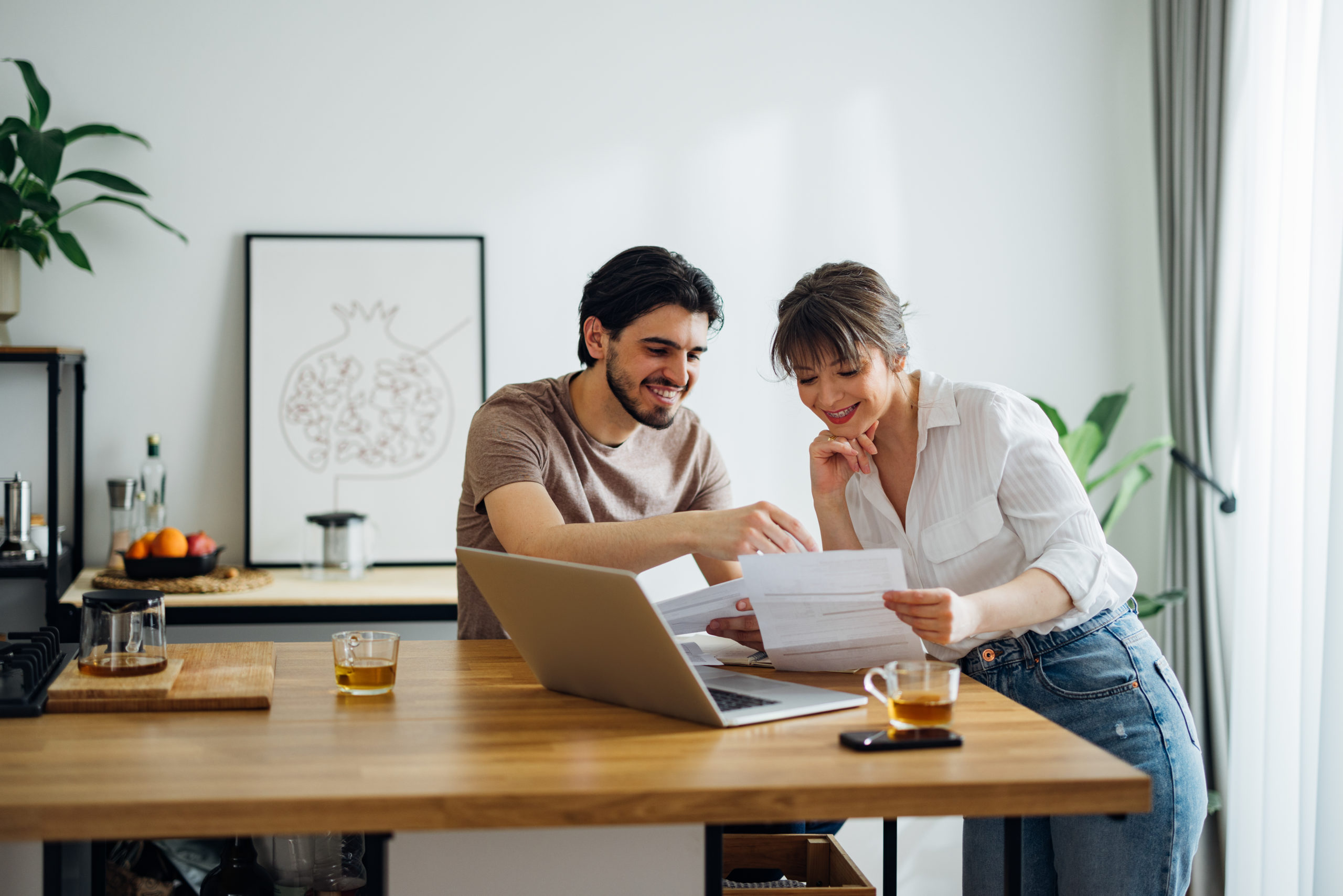 A cheerful couple going over home finances together online on a laptop computer in the kitchen.