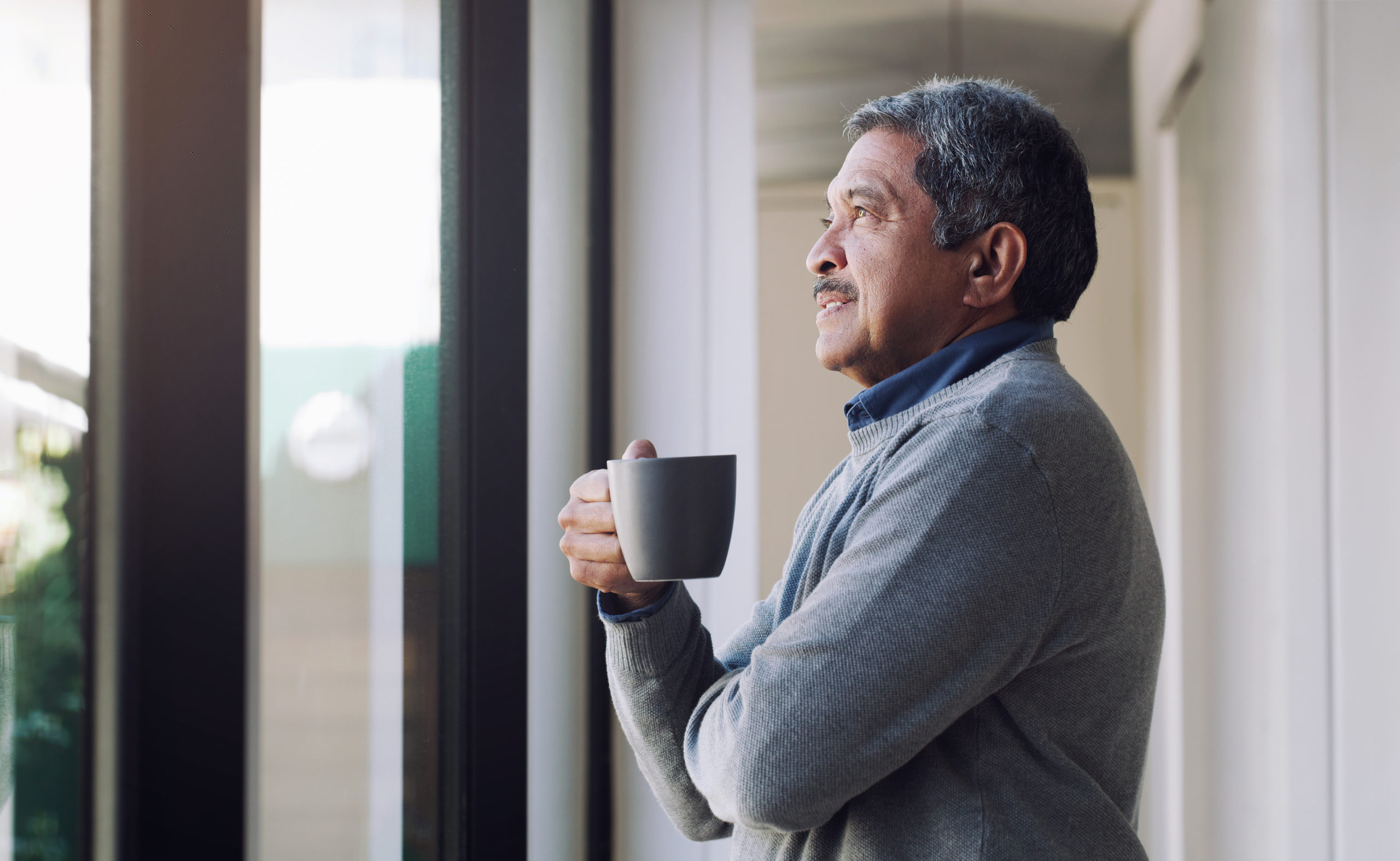 Shot of a man drinking a hot beverage and looking thoughtfully out of a window